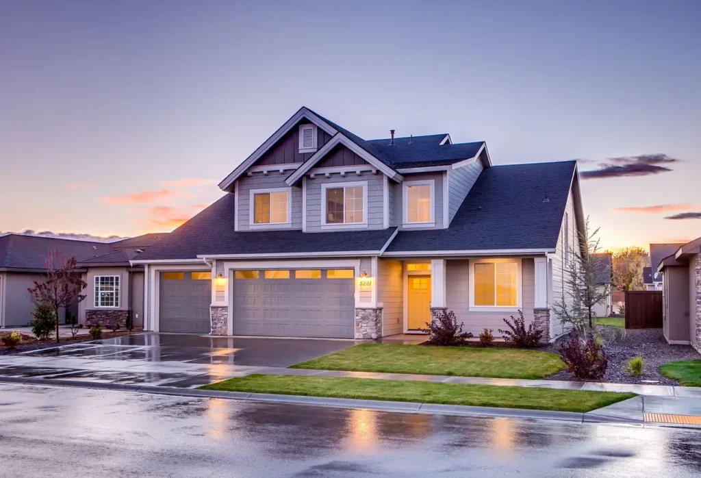 Modern two-story suburban home with gray siding and three-car garage at sunset with wet driveway