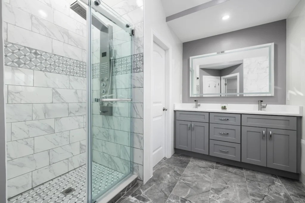 Modern bathroom with gray double vanity, white marble shower with glass door, and geometric tile accent
