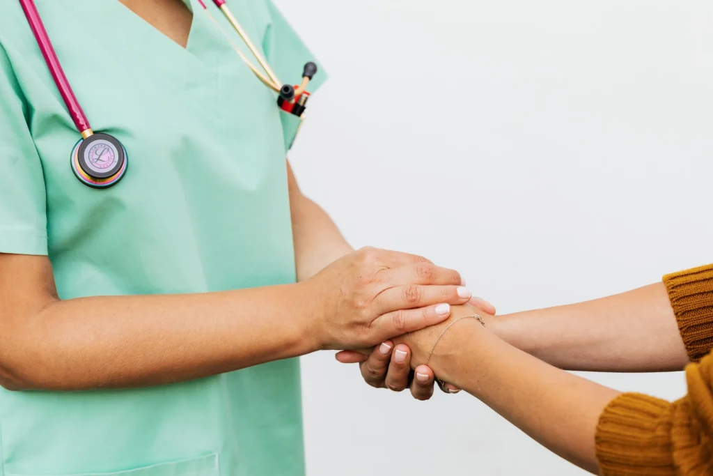 Healthcare worker in mint scrubs with stethoscope holding patient's hand in supportive gesture