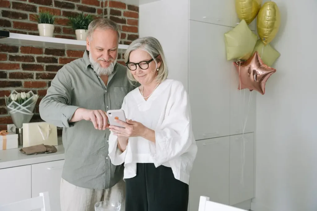 Mature couple looking at smartphone together in modern kitchen with festive balloons in background