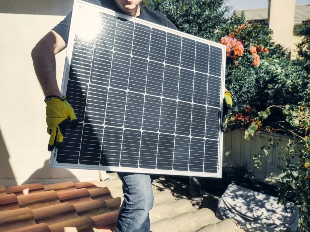 Worker in yellow gloves holding a solar panel on a residential rooftop during installation