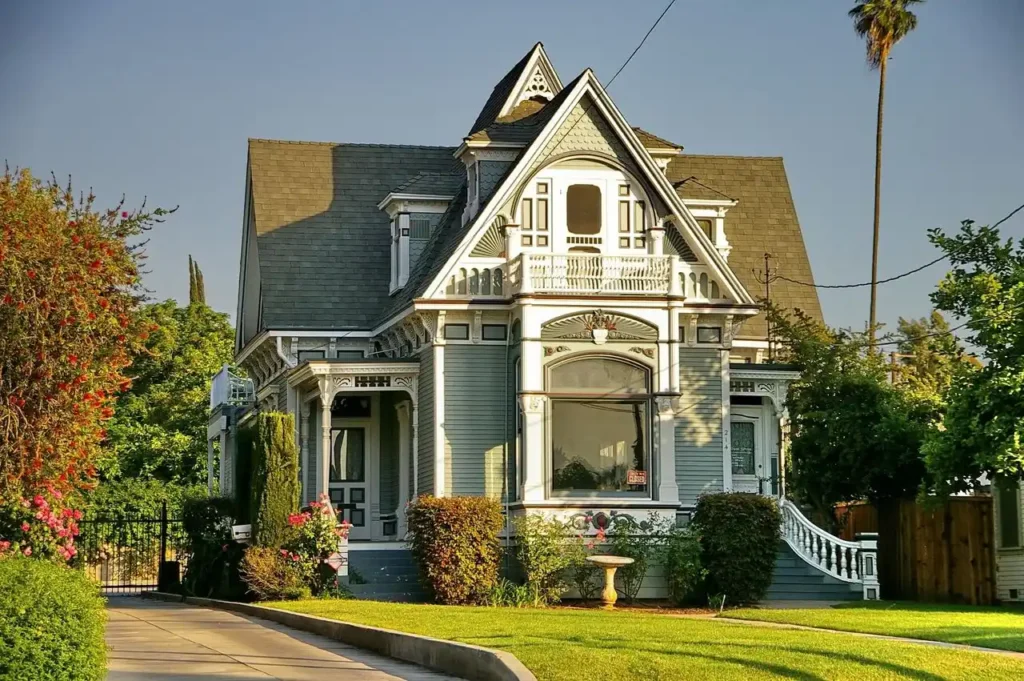 Victorian-style house with ornate white trim, blue-gray siding, steep gabled roof, and decorative balcony