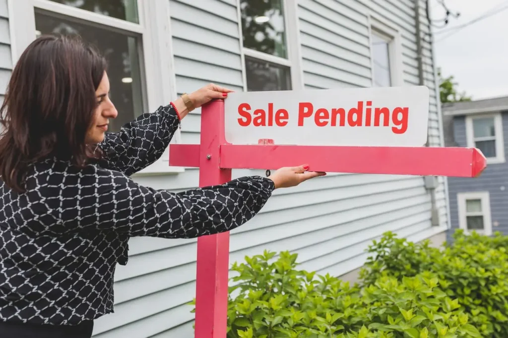 Real estate agent placing sale pending sign in front of white house exterior